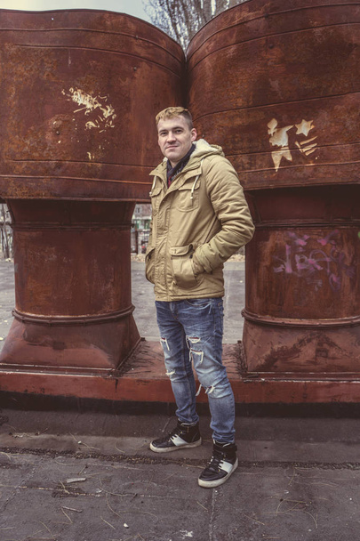 Handsome man in warm street clothes posing outside, in the background iron pipe - Фото, зображення