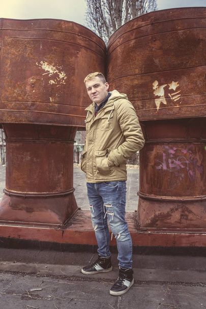 Handsome man in warm street clothes posing outside, in the background iron pipe - Foto, afbeelding
