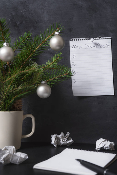 オフィスの壁に固定されたノートブックに新年の目標とリスト,机の上に紙や松の枝を粉砕.目標計画概念. - 写真・画像