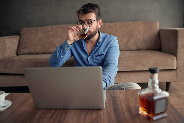 businessman is drinking whisky while working from a home at laptop   - Foto, imagen
