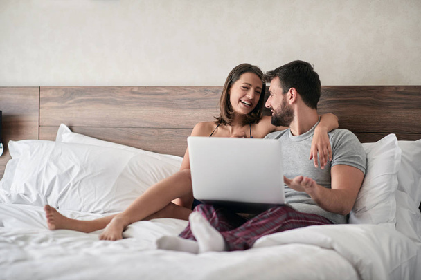 コンピューター - 人々、性的、技術コンセプトをベッドに横たわって幸せな若いカップル - 写真・画像
