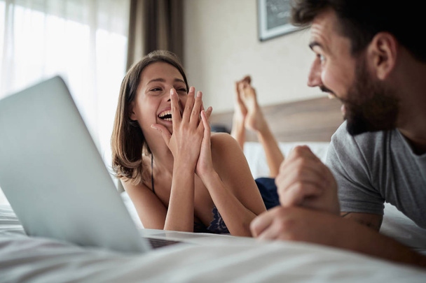people, family, bedtime and fun concept -happy young couple using laptop together in bed at home in bedroom - Foto, immagini