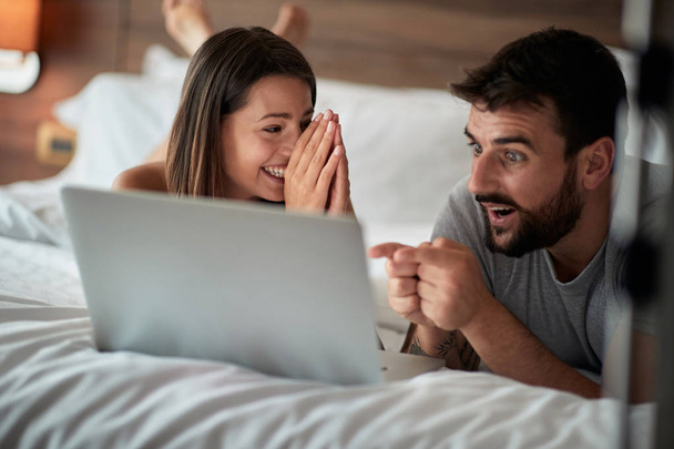 Cheerful couple using a laptop lying on their bed at home - Foto, Imagen