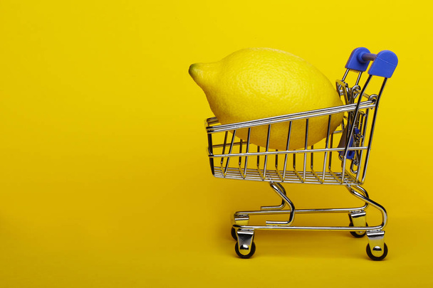 Lemon in shopping cart, shopping trolley on yellow background - Фото, зображення