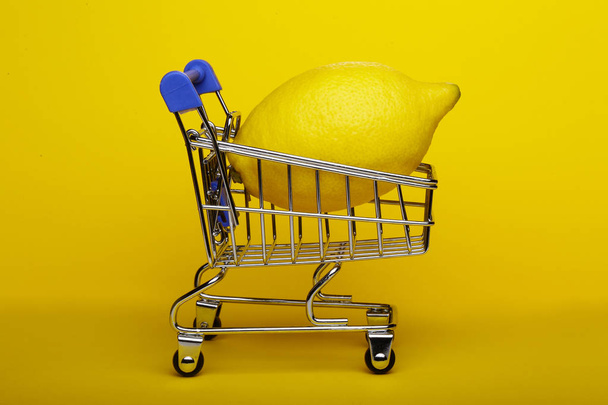 Lemon in shopping cart, shopping trolley on yellow background - Фото, изображение