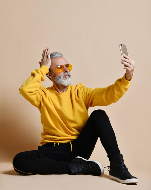 Portret van gelukkig senior miljonair man met smartphone mobiel maken selfie in gele zonnebril - Foto, afbeelding