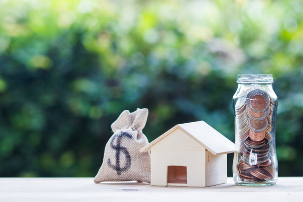 Home loan, mortgages, debt, savings money for home buying concept : US dollar in a money bag, small residential, house model on table against green nature background. Exchange of finances and houses. - Fotó, kép