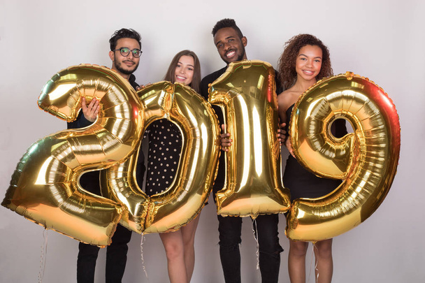 Young company of friends holding sign 2019 made of golden balloons for new year on white background. - Foto, Imagen