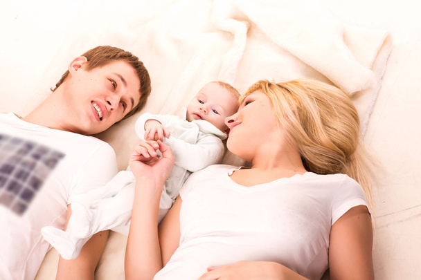 Молода щаслива сім'я: мати, батько і дитина брешуть
 - Фото, зображення