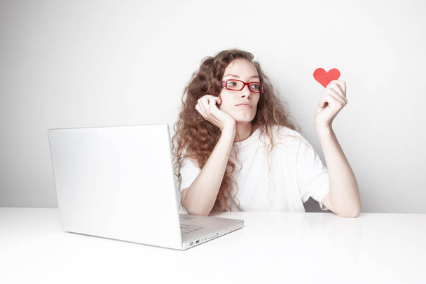 beyaz duvar önünde dizüstü bilgisayar ile çalışma ve kırmızı kalp tutan güzel kızıl saçlı kadın - Fotoğraf, Görsel