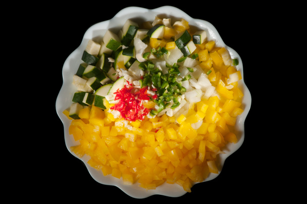 Тарелка, полная разноцветных нарезанных овощей, изолированных на черном фоне
 - Фото, изображение