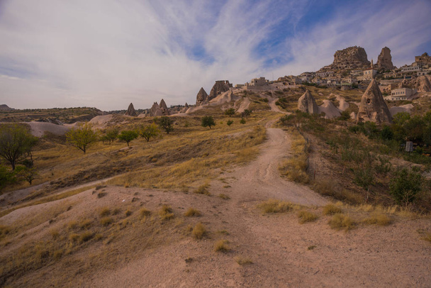 Uchisar, Cappadocia, Nevsehir province, Turkey: The road on the field goes to the city and the castle of Uchisar. Rock houses and churches. Rock houses and churches. - Photo, image