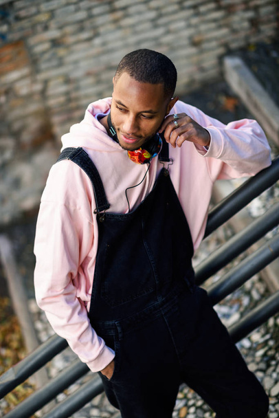 Fiatal fekete férfi alkalmi ruhában, mosolygós városi lépcsőn. Boldog afrikai fickó kantáros nadrág szabadban - Fotó, kép