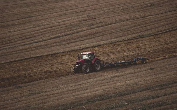 Un solo tractor arando el suelo sobre un fondo de tierra marrón
. - Foto, Imagen