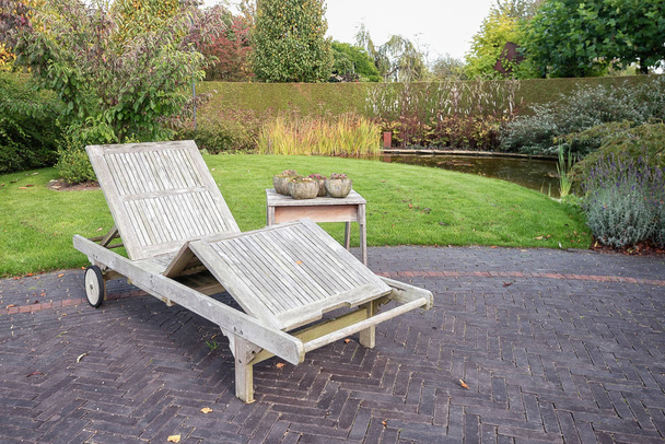 Wooden lounger to relax at the pond in the garden somewhere in an autumn park in the Netherlands. - Photo, Image