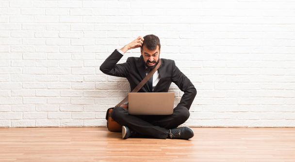 Geschäftsmann mit Laptop auf dem Boden sitzend, Zweifel am Kopf kratzend - Foto, Bild