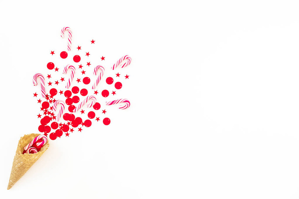 Conceito de festa de Natal com confete vermelho brilhante e cone de waffle no branco. Deitado plano, vista superior
. - Foto, Imagem