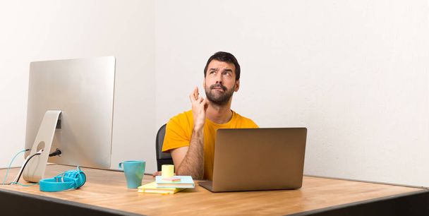 Homem trabalhando com laptot em um escritório com dedos cruzando e desejando o melhor
 - Foto, Imagem