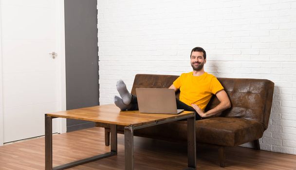 Man met zijn laptop op een kamer poseren met de armen bij de hip en glimlachen - Foto, afbeelding