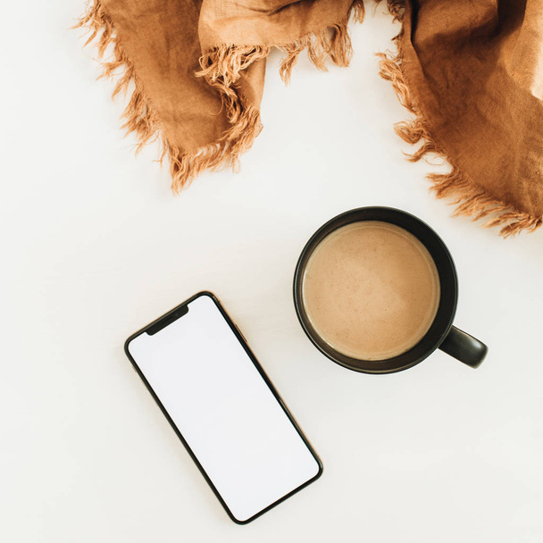 Tasse Kaffee, braune Decke und Smartphone mit leerem Bildschirm-Attrappe auf weißem Hintergrund. flache Lage, Draufsicht. - Foto, Bild