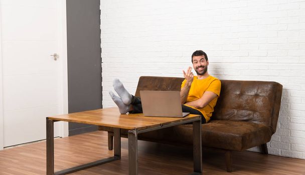 Man with his laptop in a room inviting to come with hand. Happy that you came - Foto, Bild