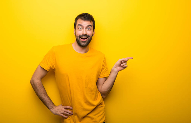 Человек на изолированном ярко-желтом цвете указывая пальцем в сторону и представляя продукт
 - Фото, изображение