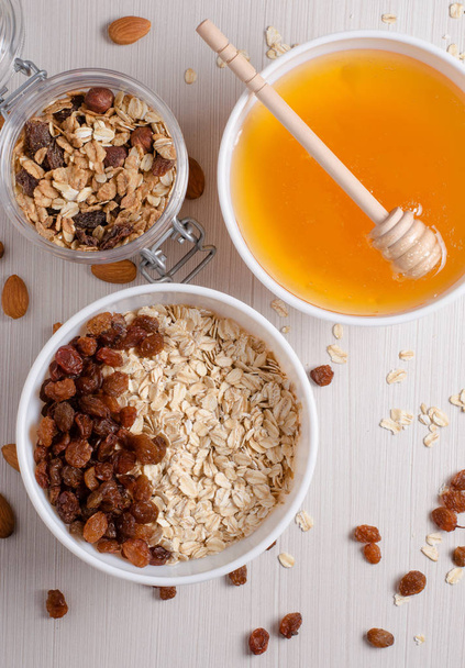 Healthy Breakfast. Oatmeal with raisins in white bowl. Almonds, honey on white  table background. Flat top view - Foto, imagen