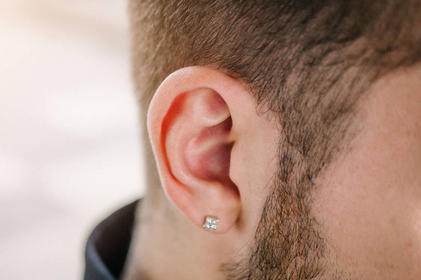 Earring in the male ear. Piercing Part of the body. Young man - Zdjęcie, obraz