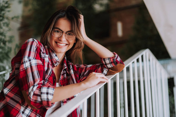Cheerful young lady in glasses posing near stair railing - Фото, изображение