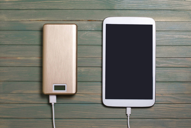 Portable power bank and tablet PC on wooden background. Flat top vie - Foto, immagini