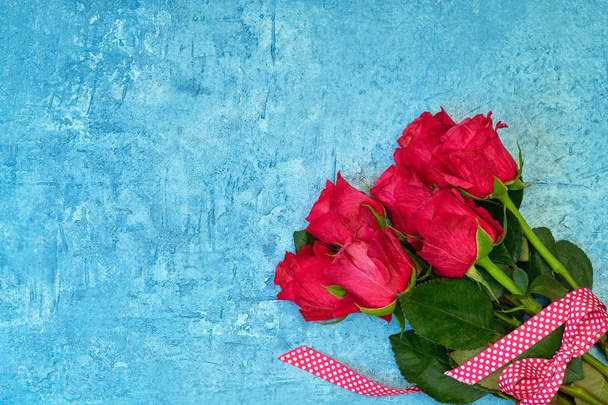 Bouquet of red roses decorated with ribbon on blue background. Top view, copy space. Greeting card - Фото, зображення