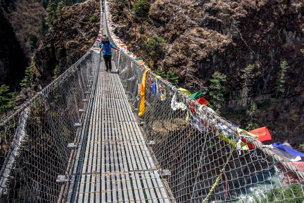Пейзаж с видом на вход на подвесной мост. Через мост проходит один альпинист. Национальный парк "Эверест", Непал
. - Фото, изображение