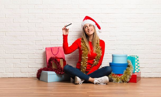 Mädchen mit Weihnachtsmütze und vielen Geschenken, die die Weihnachtsfeiertage mit einer Kreditkarte feiern - Foto, Bild