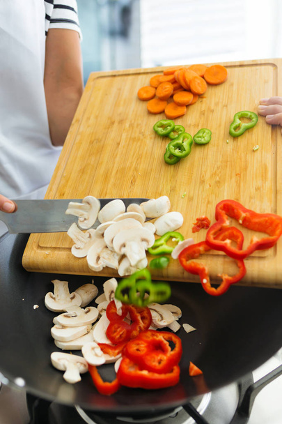 Крупный план руки здоровой женщины положить свежие овощи в кастрюлю на кухне дома
. - Фото, изображение