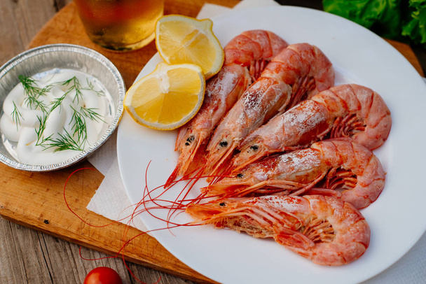 Langoustine and shrimp are grilled. The woman turns the shrimps forceps with chef tongs, sprinkles them with half-lemon juice - Valokuva, kuva