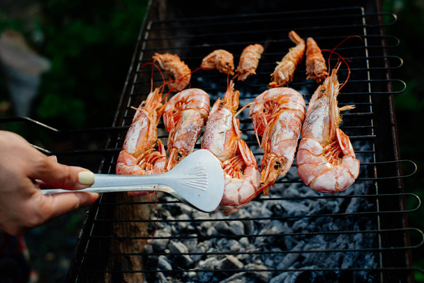 Langoustine and shrimp are grilled. The woman turns the shrimps forceps with chef tongs, sprinkles them with half-lemon juice - Foto, afbeelding