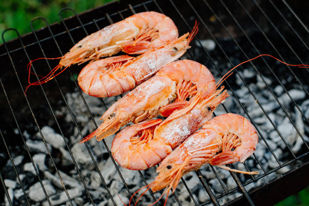 Langoustine and shrimp are grilled. The woman turns the shrimps forceps with chef tongs, sprinkles them with half-lemon juice - Valokuva, kuva