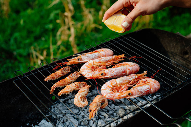 Langoustine and shrimp are grilled. The woman turns the shrimps forceps with chef tongs, sprinkles them with half-lemon juice - Fotografie, Obrázek