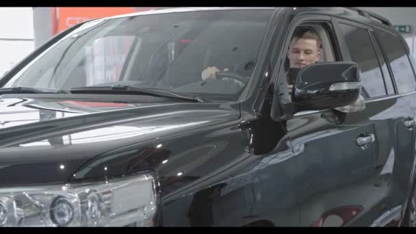 Selbstbewusster Mann sitzt in großem schwarzen Auto in Autosalon - Filmmaterial, Video