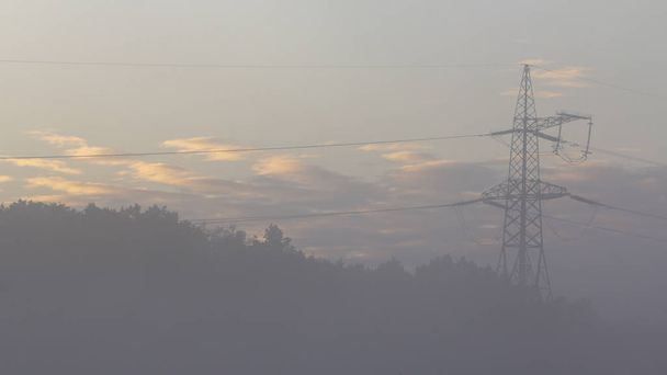 Wysokonapięciowe linie przesyłowe energii elektrycznej i słup w mglisty poranek - Zdjęcie, obraz