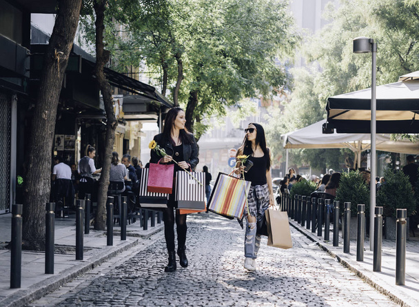 two female friends with shopping bags walking the city streets - Photo, Image