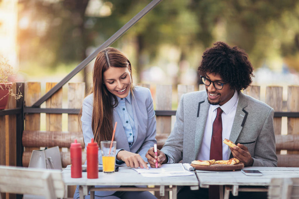Feliz equipo de negocios jóvenes comiendo pizza en la cafetería al aire libre.Concepto de negocios, comida y gente
. - Foto, Imagen