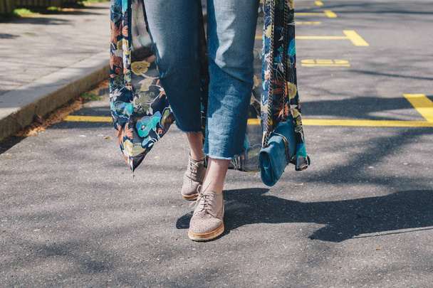 Elegante donna con jeans in denim, scarpe beige, abito floreale in kimono, attraversando la strada dondolando la sua borsa in pelle scamosciata blu
 - Foto, immagini