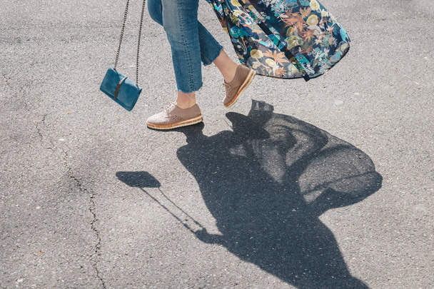 Elegante donna con jeans in denim, scarpe beige, abito floreale in kimono, attraversando la strada dondolando la sua borsa in pelle scamosciata blu
 - Foto, immagini