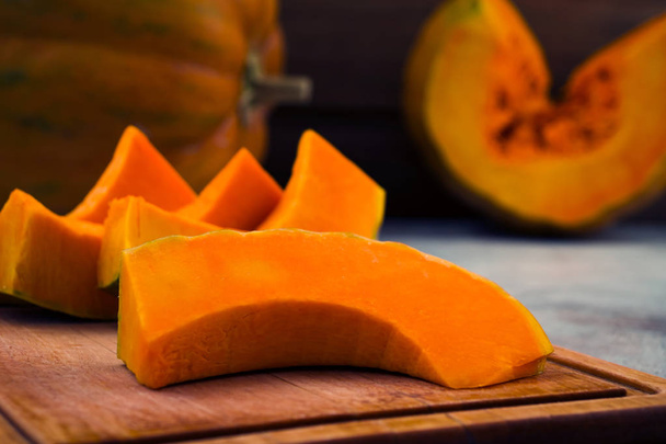 Sliced ripe pumpkin. Vegan and raw food. Vegetable diet. Close up. Wooden board. Light background. - Photo, Image