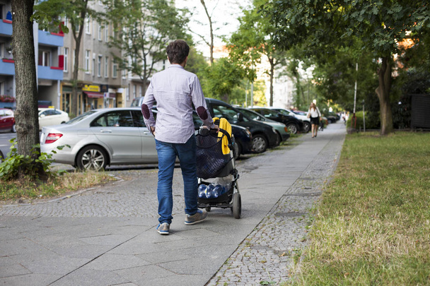 Young dad walking with a baby carriage on sidewalk - Fotoğraf, Görsel