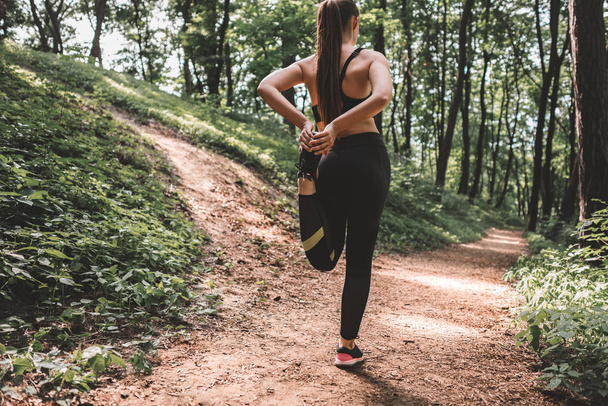 Full length image of young woman athlete making warm-up before training in the woods. Back view of a slim fit female preparing to run on forest path - Φωτογραφία, εικόνα