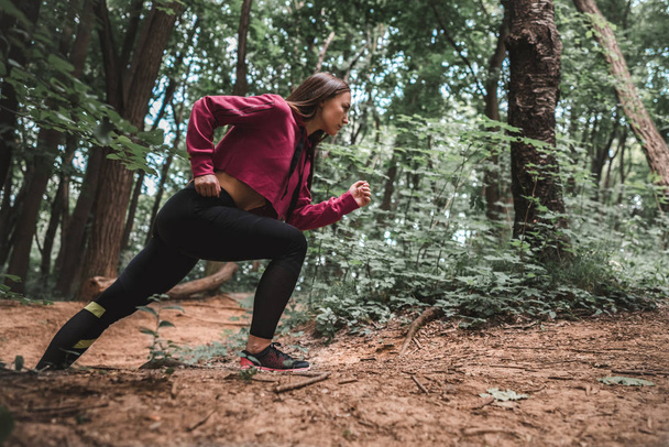 Side view of a young sporty girl overcomes steep climbs on training in the forest. Full length shot of a confident female athlete climbing a forest trail. - Photo, Image
