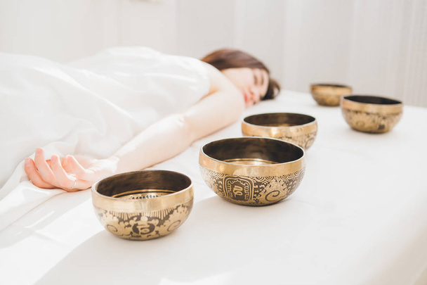 Young beautiful girl doing massage therapy singing bowls in the Spa. The concept of relaxation and alternative medicine. Toning. - Valokuva, kuva