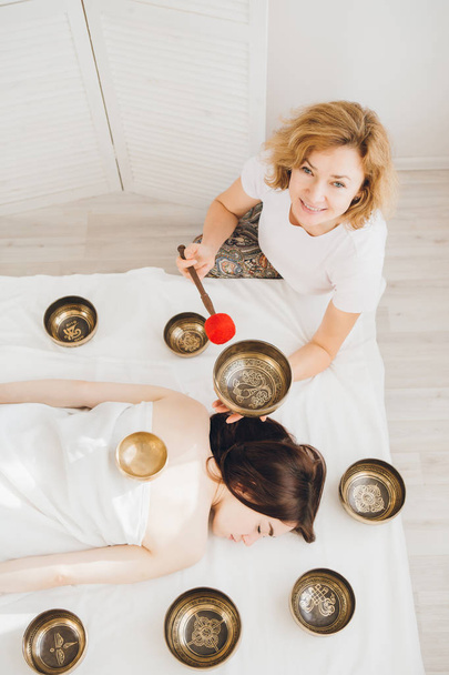 Young beautiful girl doing massage therapy singing bowls in the Spa. The concept of relaxation and alternative medicine. Toning. - Photo, image